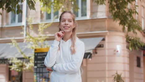 thoughtful smiling young woman with pensive expression touching chin looking around on city street