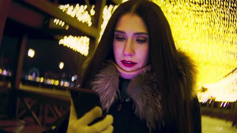 woman using phone at night in a city with christmas lights