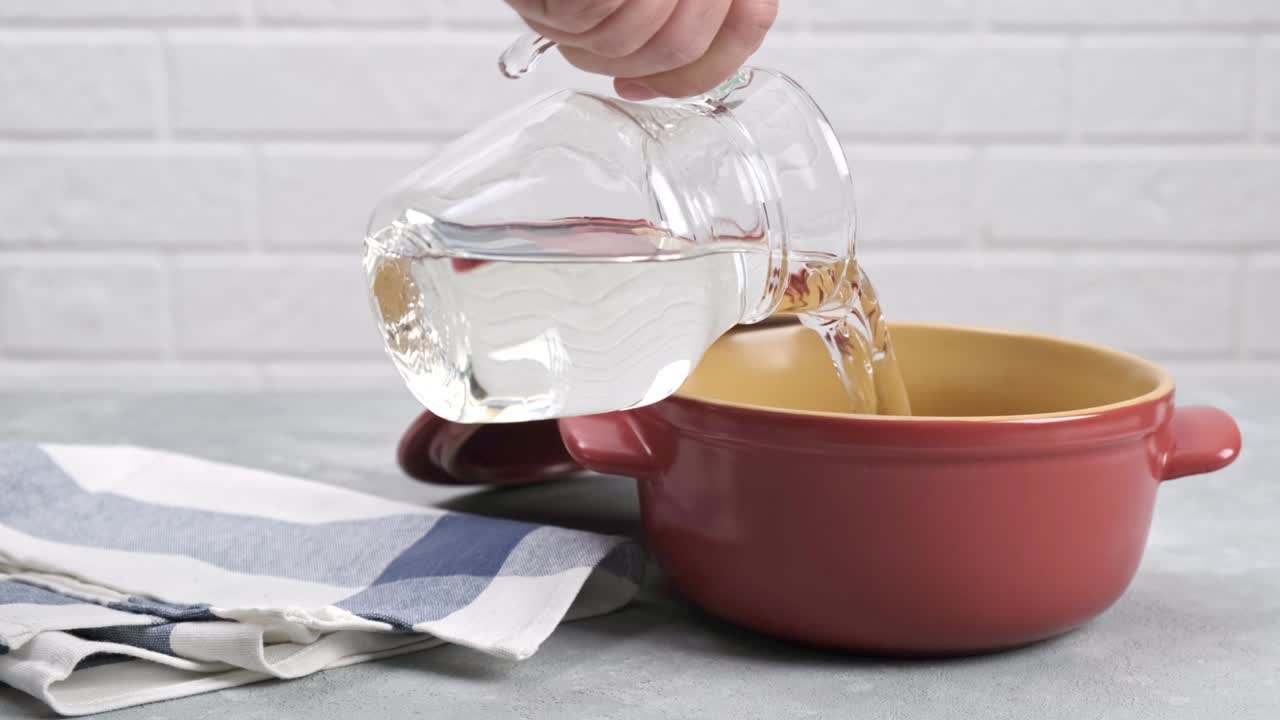 Pouring clean water from a glass jug into a pot.