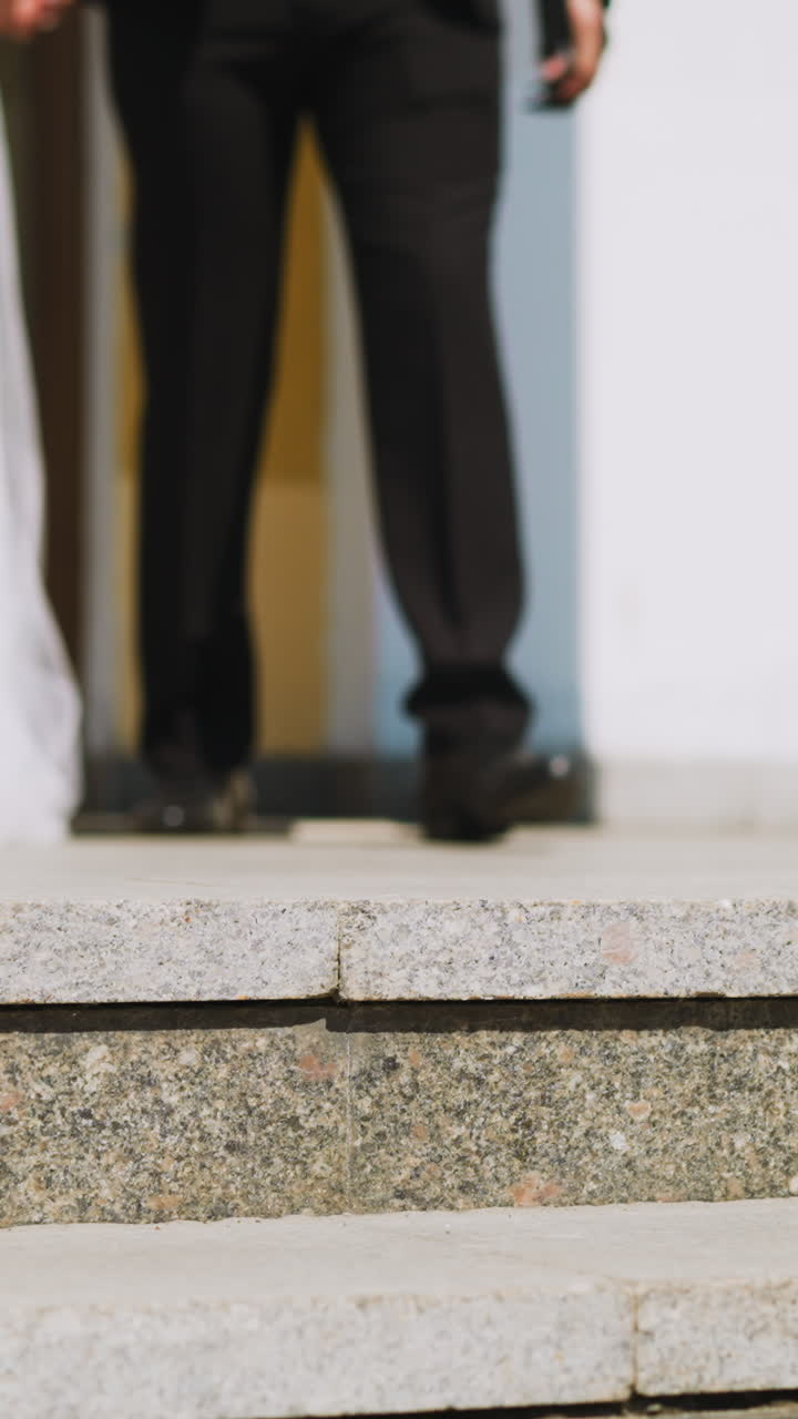 Happy newlywed woman wearing white dress and groom in dark suit walk to stairs at building in city street on summer day closeup slow motion