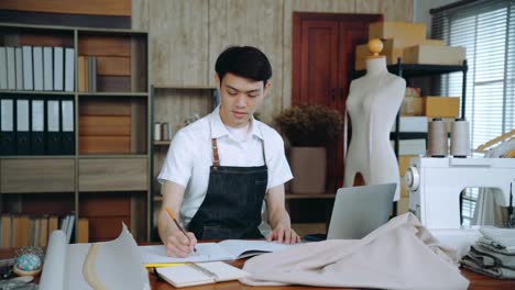 asian young male fashion designer sketching out new fashion collection. small business starts up designer, clothing shop owner, freelancer work at home. dressmakers working on clothes creation.