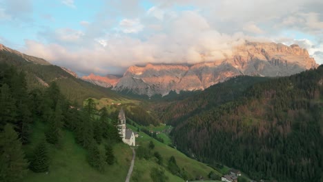 Luftaufnahmen-Des-Dorfes-La-Val-Am-Abend-Mit-Dem-Majestätischen,-Wolkenverhangenen-Berg-Sas-Dles-Nü-Im-Hintergrund