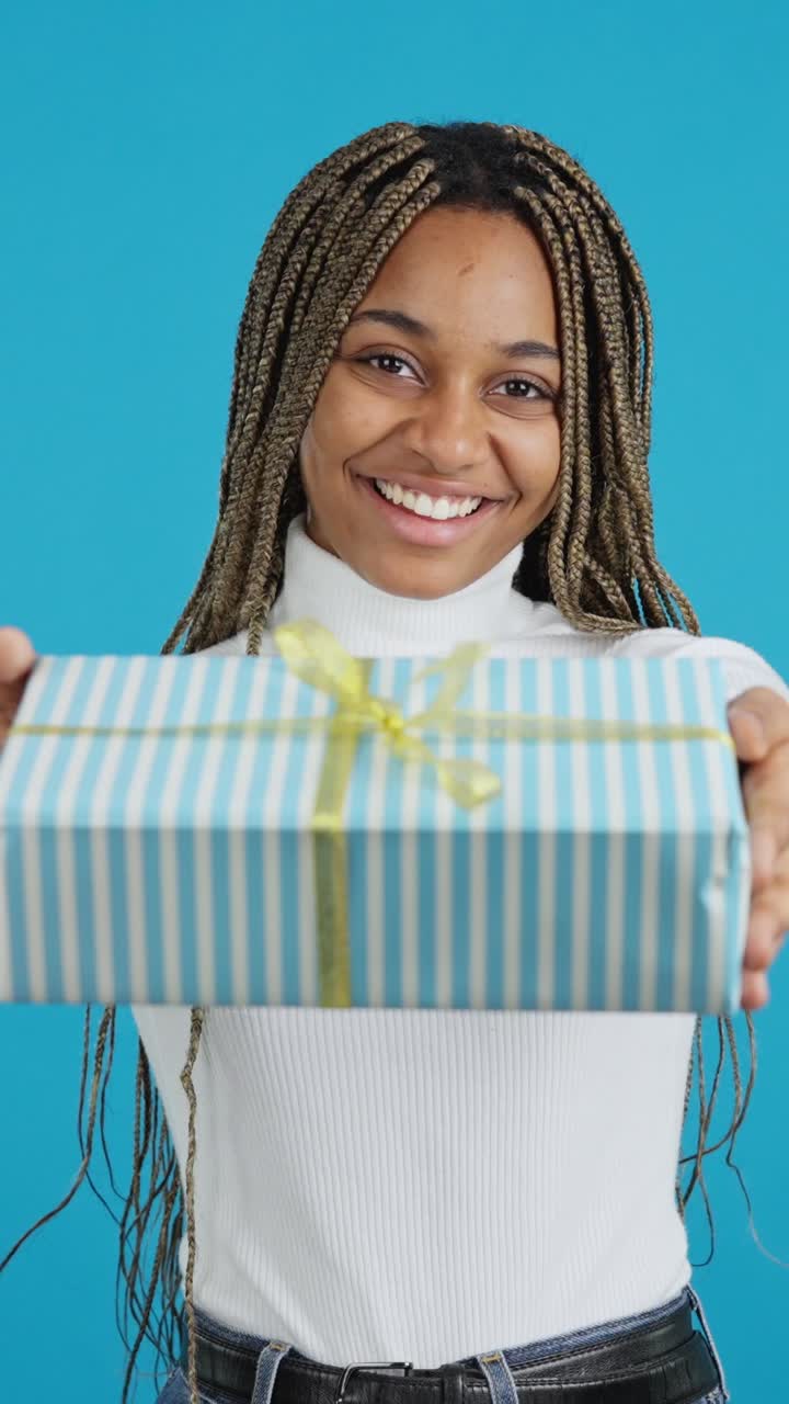 A happy woman smiles while holding out a striped gift box