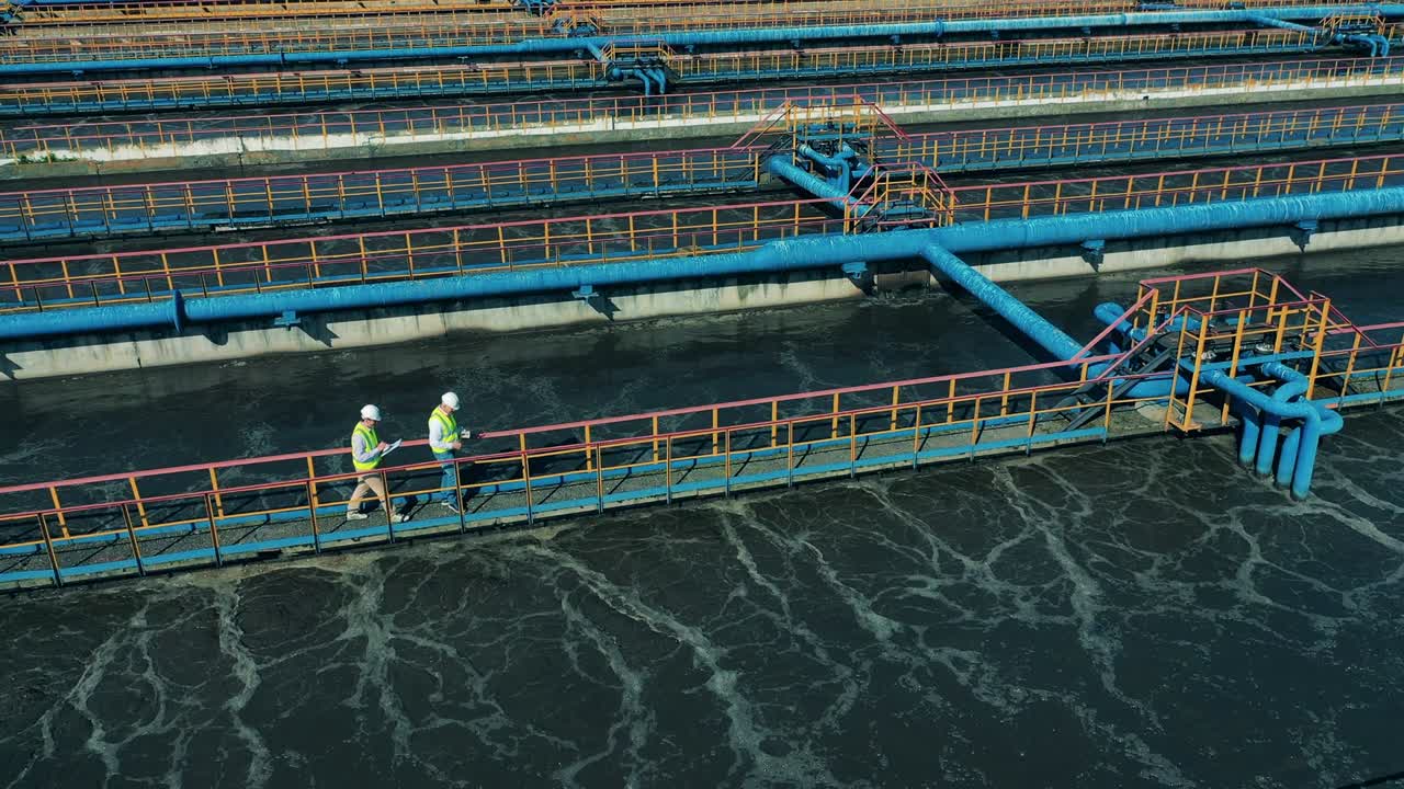 trabajadores caminando a lo largo de las tuberías en una planta de tratamiento de aguas residuales
