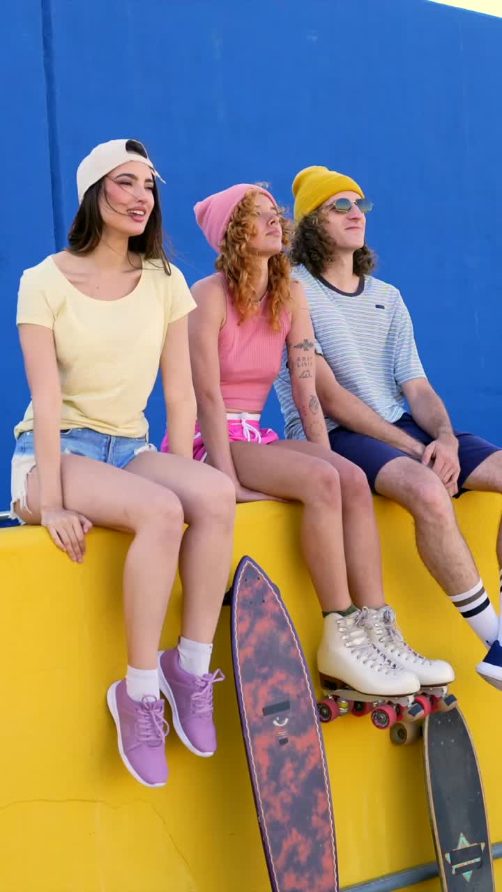 Group of Stylish Young Adults Sitting on a Colorful Wall with Skateboards