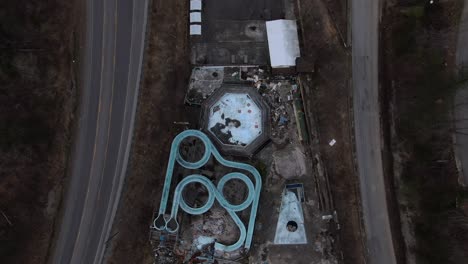 top down aerial drone footage of an abandoned, overgrown water park with slides and swimming pools