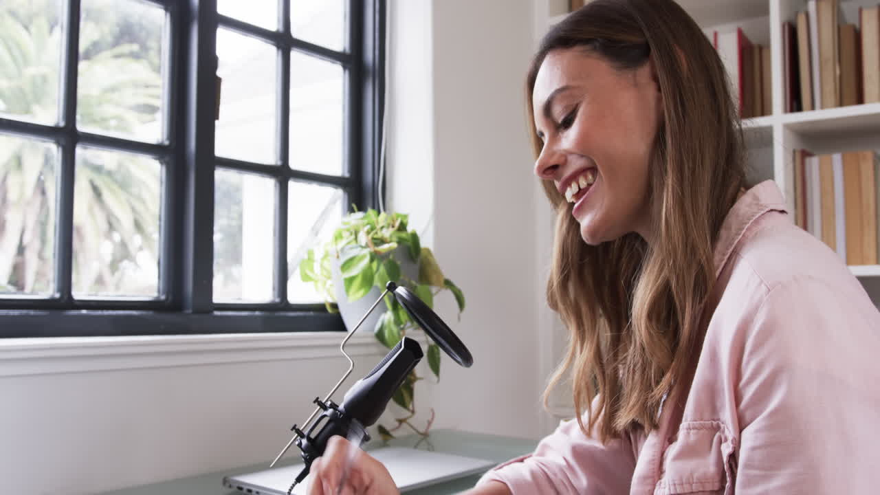 Smiling woman recording podcast at home with microphone and laptop