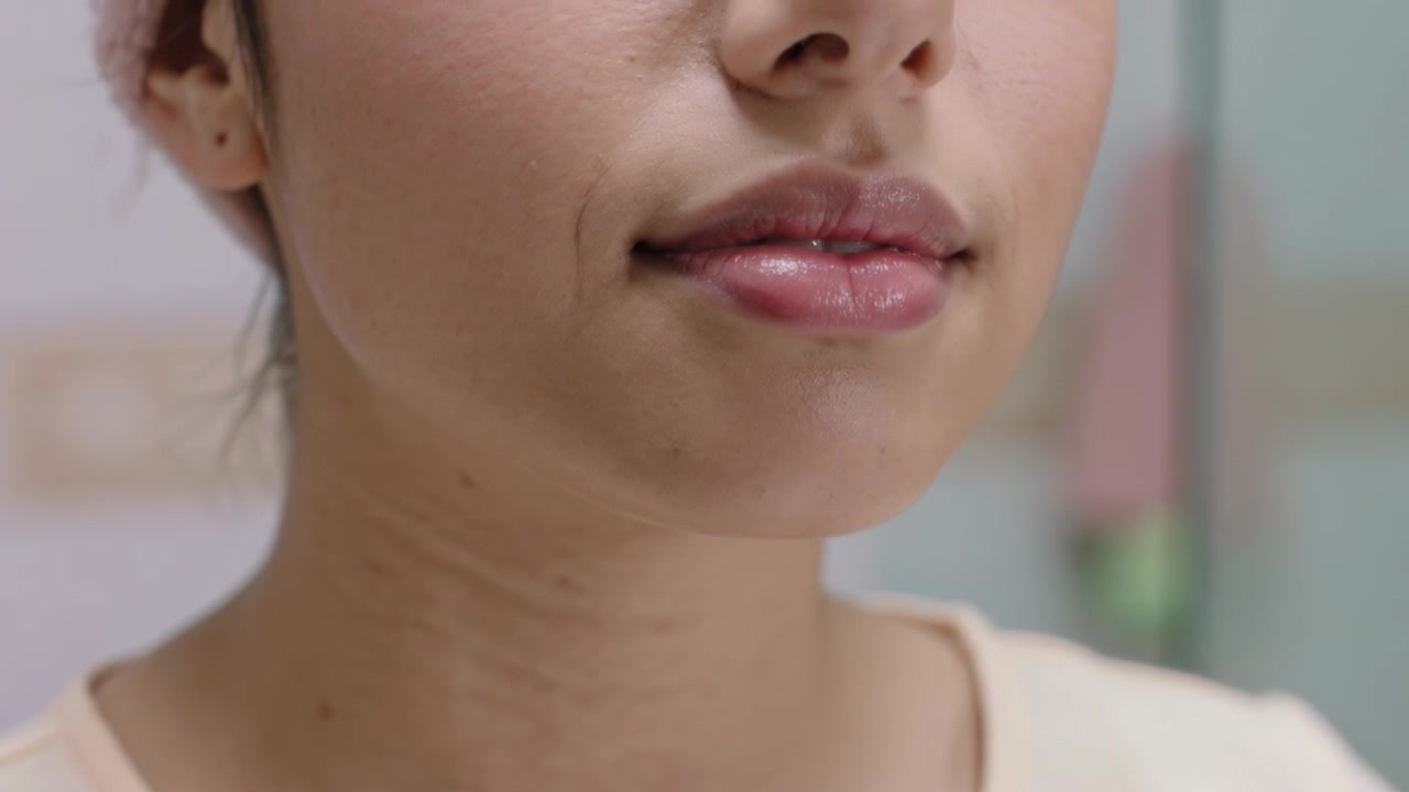 Una donna con un tubetto di balsamo labbra bianco lo applica sul labbro inferiore davanti allo specchio del bagno, controllando le labbra.