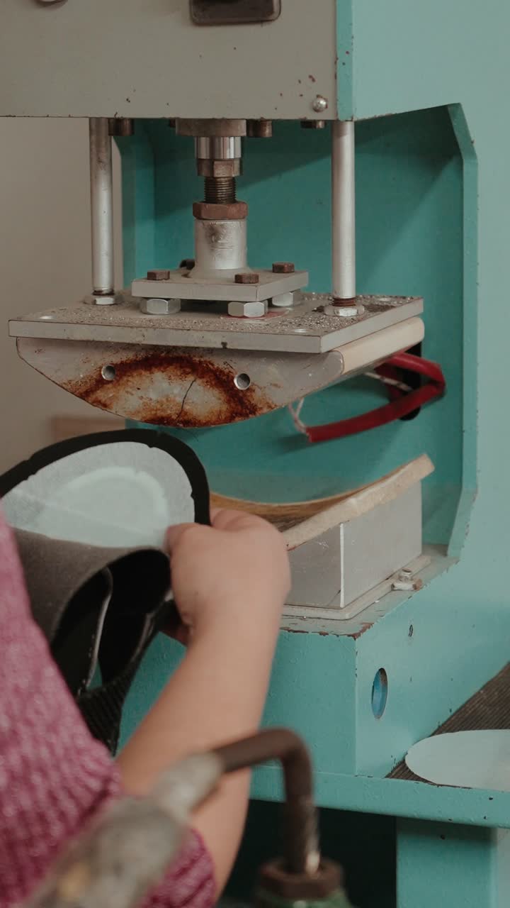 Vertical closeup of artisan shaping leather pieces in footwear production