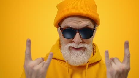 un anciano alegre posando en el estudio. un tipo alegre mostrando un gesto de rock en el interior.