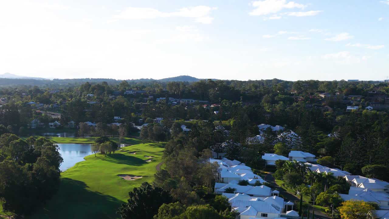 Aerial footage captures a scenic golf course surrounded by lush greenery and water features under bright daylight