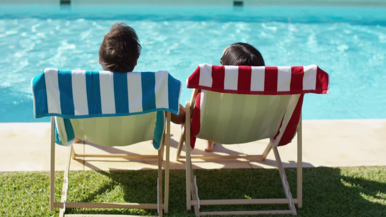 Couple relaxing in colorful deck chairs poolside