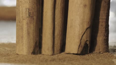 slow motion shot of cinnamon sticks fall over brown powder in table, close up