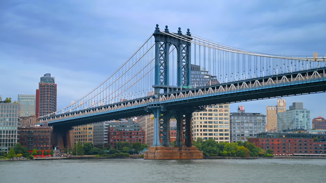 Stunning Manhattan Bridge against gloomy grey cloudy sky. Low angle view from the riverscape. Skyline of New York at backdrop