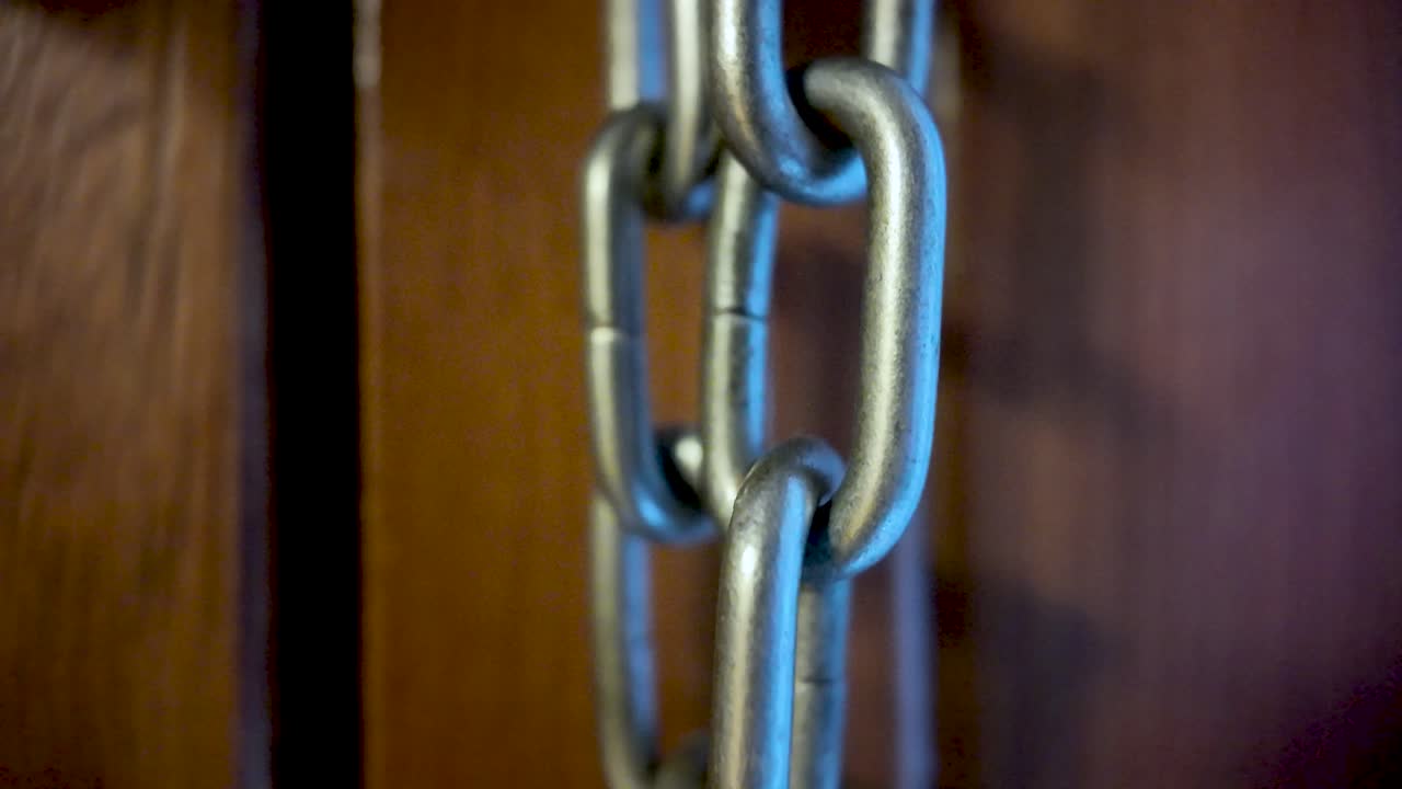 Close-up of a metal door chain and lock on wooden door, emphasizing security hardware and access control