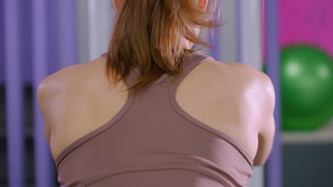 close up rear view of young woman in brown activewear slightly bent forward, engaging in weight training exercise using cable machine in gym