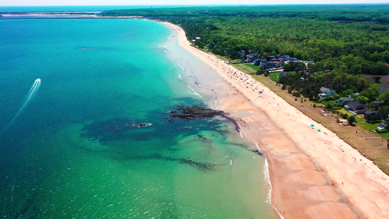 Aerial bird’s-eye drone shot looking straight down on bustling Saco beaches in Maine. Crowds spread out on sandy shore near vacation homes as Atlantic Ocean waves crash along scenic New England coast