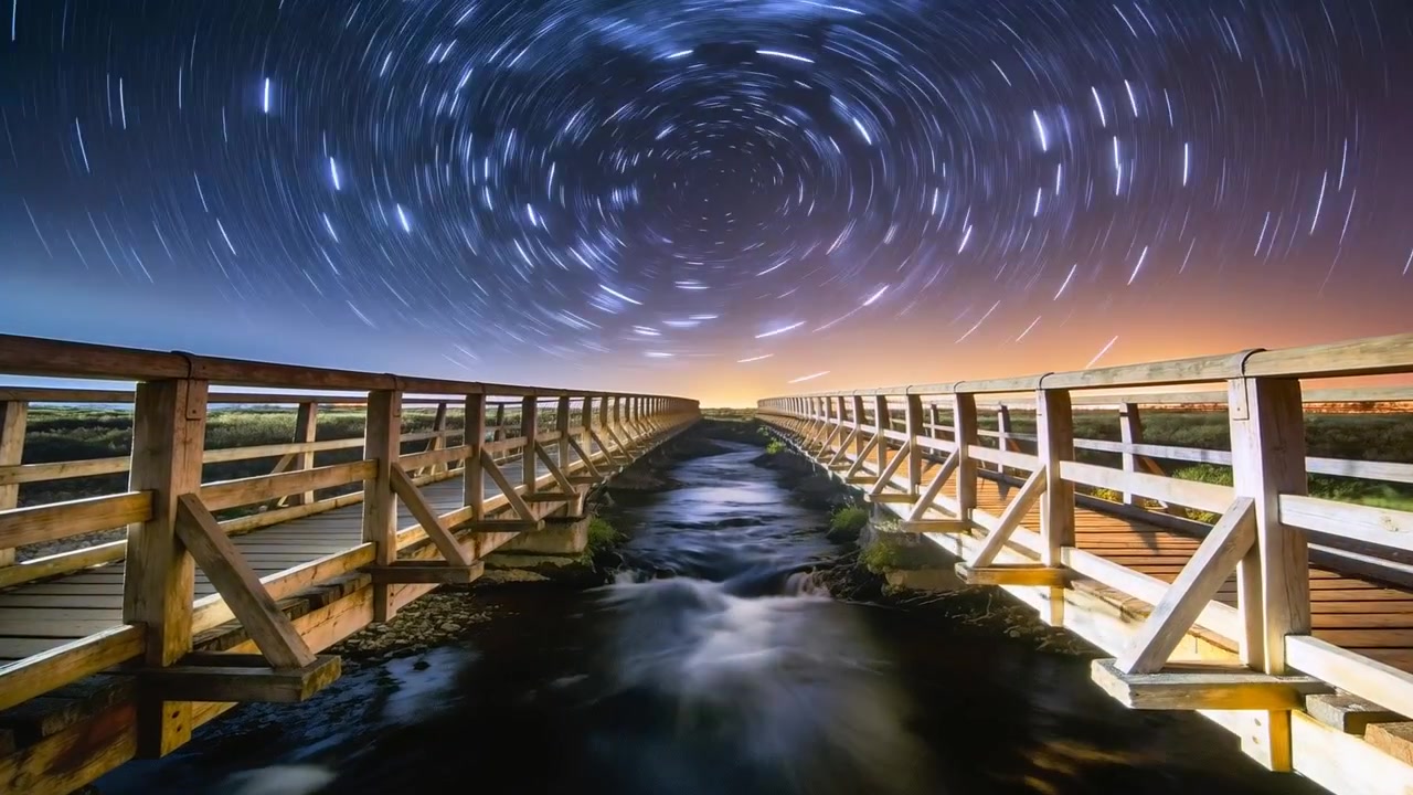 Enmarcando puentes de madera sobre un arroyo hacia el horizonte de noche, con estelas de estrellas girando, mostrando el paso del tiempo.