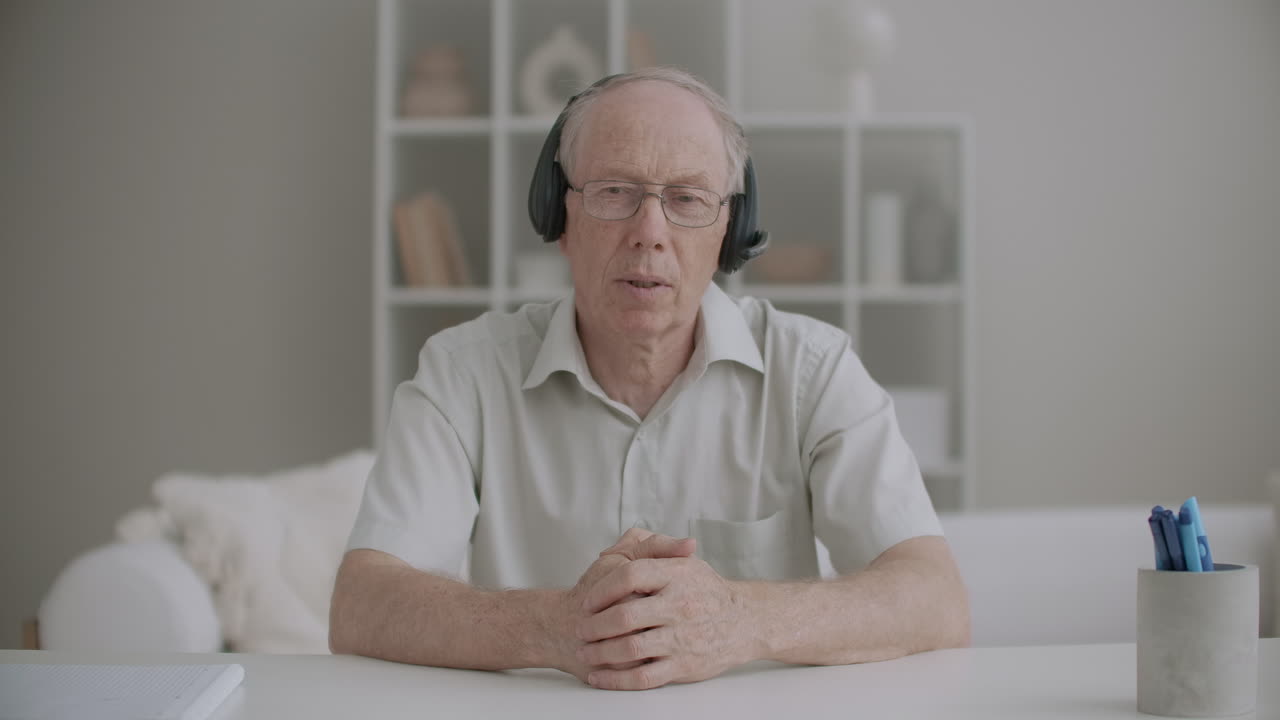 hombre de edad con auriculares está mirando a la cámara saludando a la audiencia en línea y comenzando a aprender webinar
