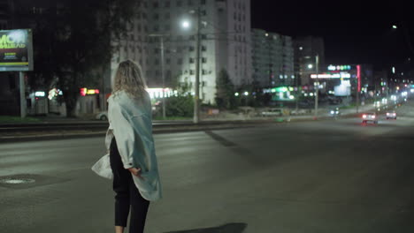 cheerful woman in white coat joyfully walks and spins along city street at night with coat floating, surrounded by softly blurred billboards, glowing car lights, and illuminated urban structures