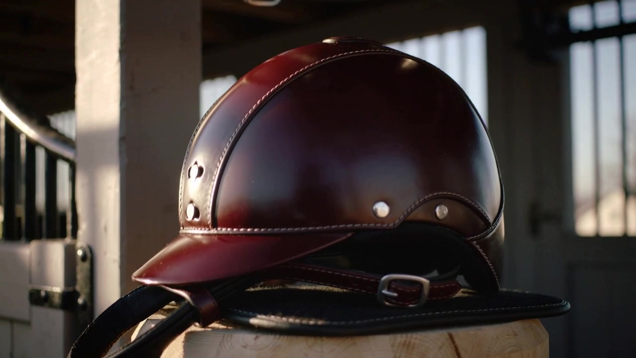 Casco de equitación de cuero brillante colgado en un poste en un establo, mostrando las hebillas.