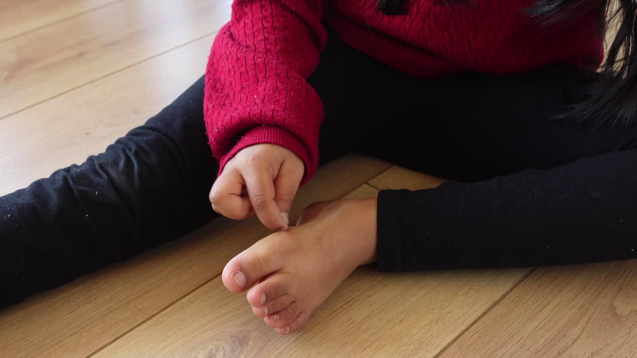 Liten flicka sitter barfota på ett trägolv