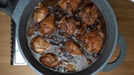 chicken pieces simmering in liquid dark sauce while reducing the sauce