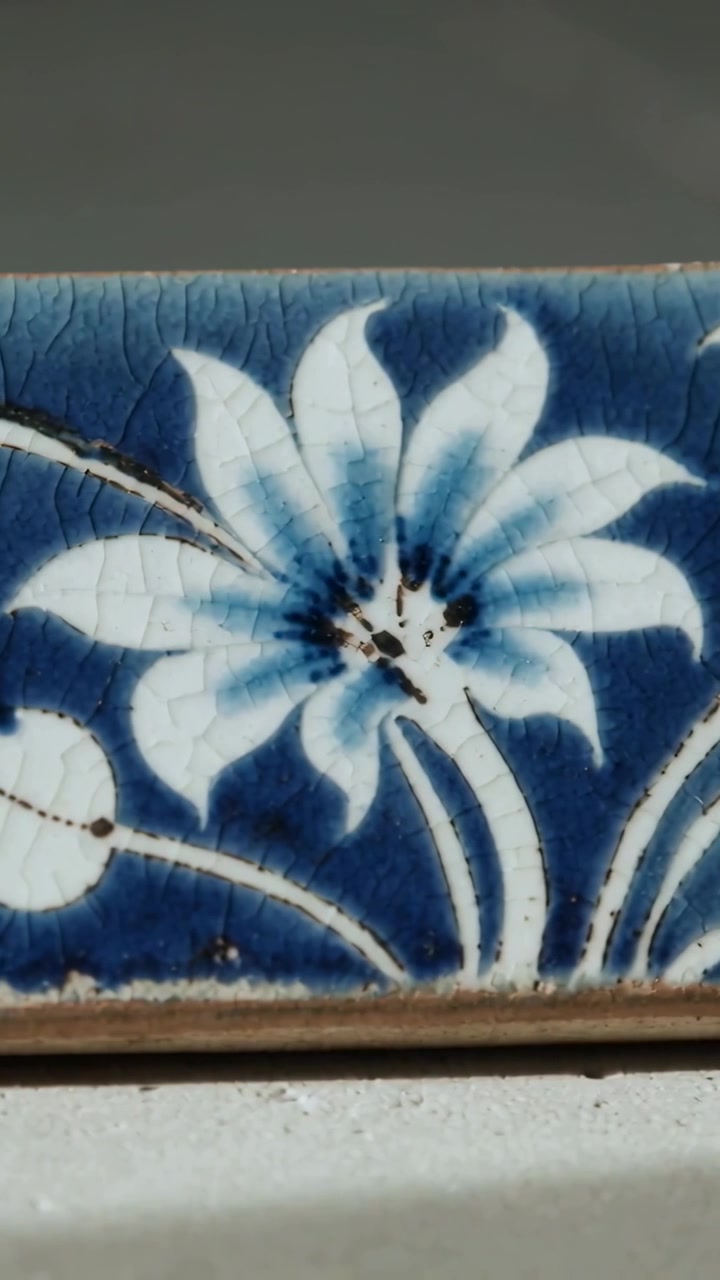 Video verticale: Telecamera che panoramica verso destra su una piastrella da parete smaltata, rivelando un fiore bianco, craquelé.