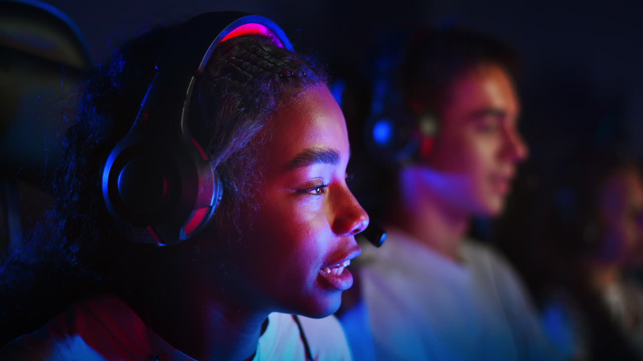 Adolescente negra con auriculares jugando a videojuegos en un club de videojuegos con iluminación azul y roja, hablando en un chat de voz. Cámara lenta