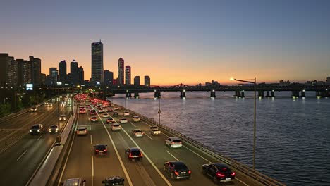 Tráfico-En-La-Autopista-Olympic-Daero-Con-El-Puente-Hangang-Y-El-Rascacielos-Cuadrado-63-Durante-La-Puesta-De-Sol-En-Seúl,-Corea-Del-Sur