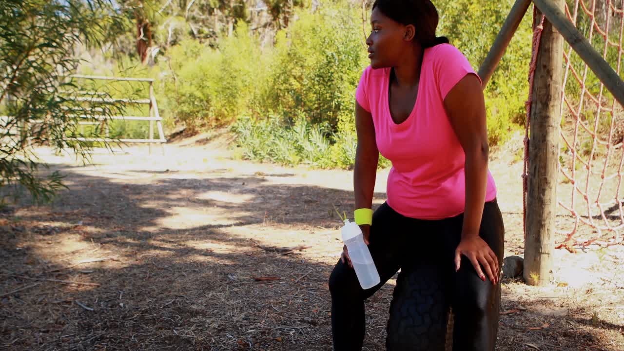 mujer bebiendo agua mientras se relaja en el neumático durante una carrera de obstáculos