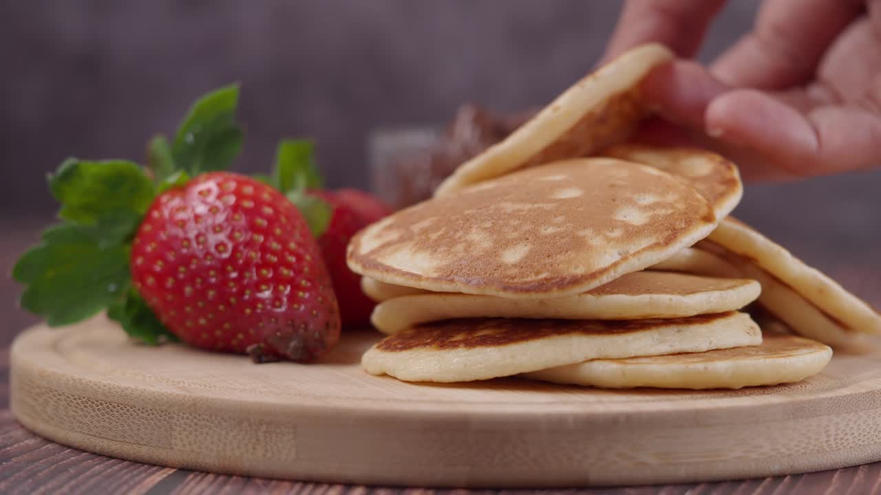 Mão empilhando pequenas panquecas com morangos frescos