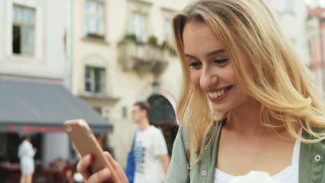 close-up view of caucasian blonde woman texting on the smartphone while walking down the street and holding coffee to go