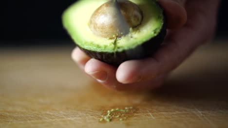 caucasian male hand holding halved avocado and taking out its pit with sharp chefs knife, slow motion