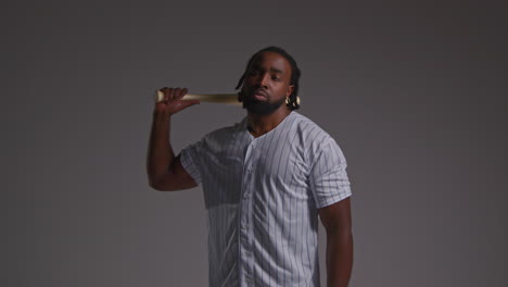 retrato de estudio de un jugador de béisbol masculino serio con una camiseta del equipo sosteniendo un bate girando disparado contra un fondo gris