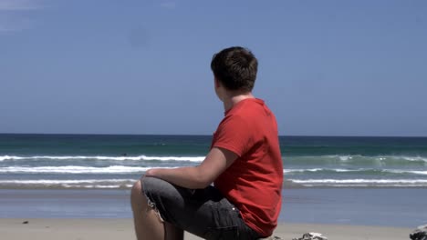 Hombre-En-Contemplación-Sentado-En-La-Orilla-De-La-Roca-De-La-Playa,-Mirando-Al-Paisaje-Marino-De-Las-Olas-Del-Océano