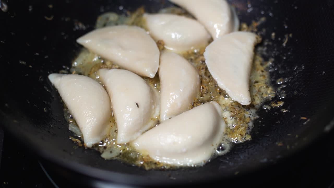 pirogies o pelmeni que se fríen mientras se arrojan más pirogies en una sartén caliente