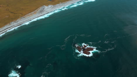 aerial view of a rocky coastline with waves crashing on the shore and a grassy landscape