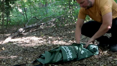 zoom en vista de un turista que enrolla una carpa en el campamento forestal y empaca para irse
