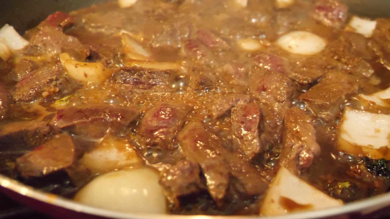 Meat and broccoli sizzling in a skillet, close up showing the bubbling of the juices