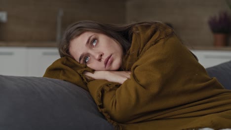 caucasian sad woman sitting on the sofa and covering the blanket at home.