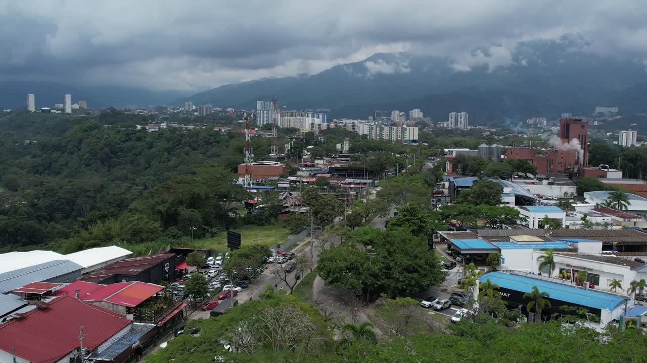 A cinematic drone shot capturing the city of Ibague on the horizon as the drone pulls back over the lush vegetation of Mirolindo roundabout