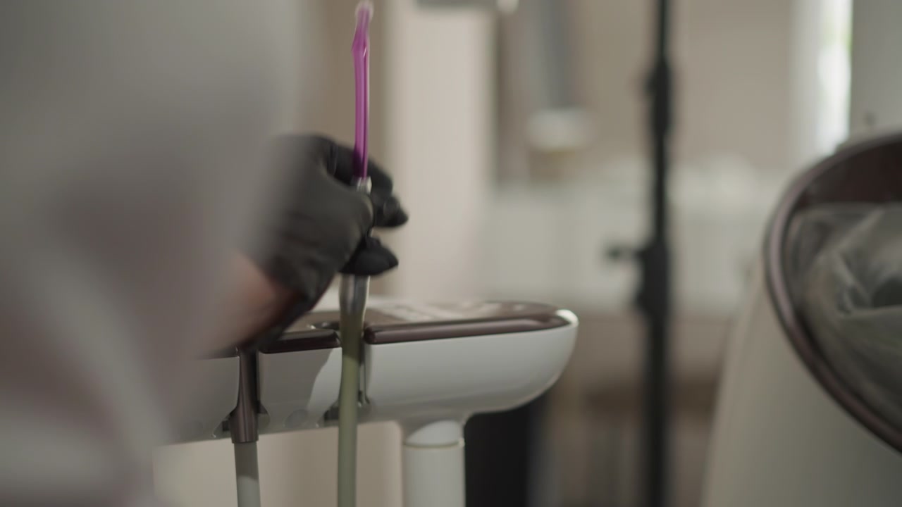 Primo piano di un professionista dentale che indossa guanti neri e maneggia strumenti ortodontici su un vassoio bianco in un ambiente clinico interno. La persona manipola vari strumenti, inclusi quelli in metallo e viola