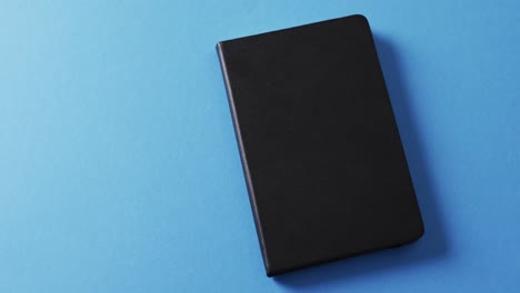 Close-up-of-closed-black-book-with-copy-space-on-blue-background-in-slow-motion