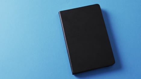 primer plano de un libro negro cerrado con espacio de copia en un fondo azul en cámara lenta