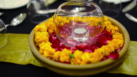 casarse con flores doradas y pétalos de rosa colocados en el plato con velas en el vaso en la mesa del comedor
