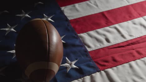 low key lighting studio shot of american football rolling onto stars and stripes flag