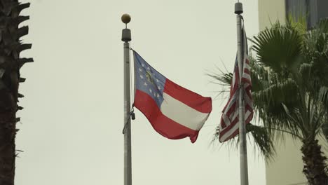 Georgia-and-United-States-flag-flapping-in-wind-with-palm-trees-and-building