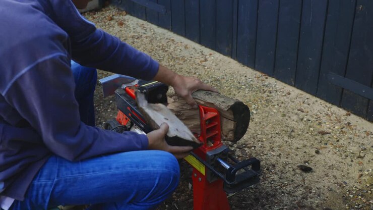 Man using log splitting machine and putting split log into wheelbarrow of wood