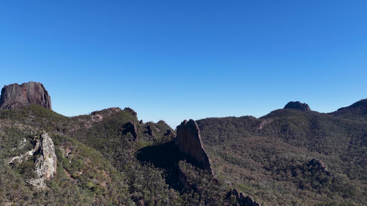 Inquadratura ampia di antiche cime vulcaniche e foresta di eucalipti sotto un cielo azzurro limpido in Australia.